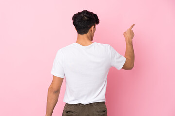 Young Argentinian man over isolated pink background pointing back with the index finger