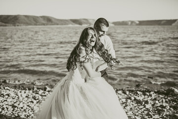 Fototapeta na wymiar bride and groom in wedding dress happy and laughing run together against rays of setting sun in summer Bakota, Ukraine