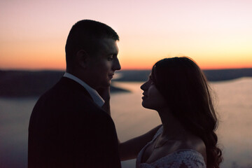 Silhouettes of bride and groom in wedding dress at night against backdrop of large lake and islands. Bakota, Ukraine