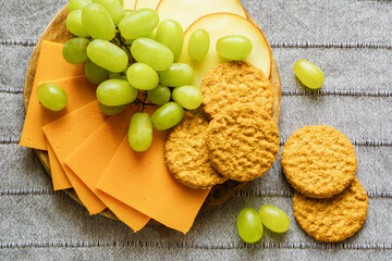 Cheese, green grapes and biscuits on the wooden tray on the gray table cloth