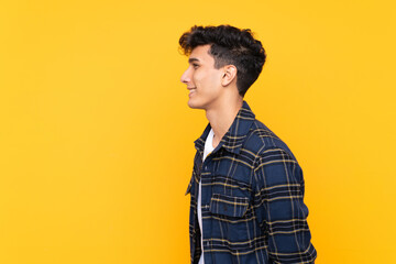 Young Argentinian man over isolated yellow background looking to the side