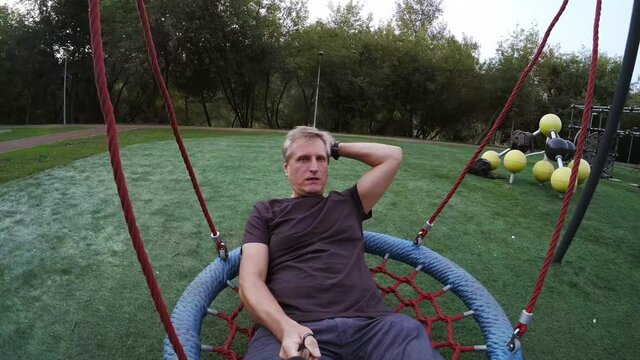 Man swinging on playground and talking at camera