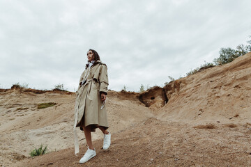 Pretty young asian girl going down from the sand quarry in a beige trench coat.
