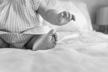 6 month old baby wearing gingham dress sitting up on bed; hand and foot reaching