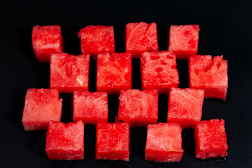 Diced slices of ripe watermelon are placed on a dark surface.