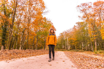 Fototapeta premium Lifestyle, a young brunette in a yellow jacket walking in a forest in autumn. Artikutza Forest in San Sebastián, Gipuzkoa, Basque Country. Spain