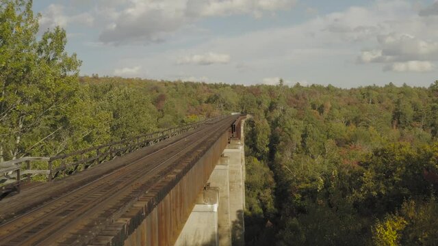 Flying through the trees along the side of a rusty railroad trestle during an early fall golden hour AERIAL