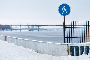 In the foreground: «Pedestrian walkway» traffic sign. In the background: Winter landscape with...