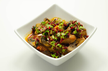 A thick stew of meat, potatoes, mushrooms, and mix of peppers served in a white bowl