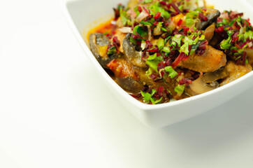 A thick stew of meat, potatoes, mushrooms, and mix of peppers served in a white bowl
