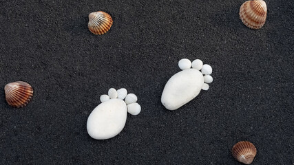 Arrière-plan grains de sable de mer, sable fin noir de plage. Emplacement pour texte. Galets en forme de petit pied pour annoncer une naissance.	