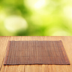 Brown bamboo food placemat on wooden table against defocused green background.