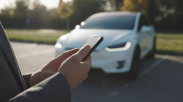 Person controls a self-driving electric car using mobile application. Autonomous autopilot driverless car. Smartphone app. Sensor scanning road ahead for vehicles, danger, speed limits.