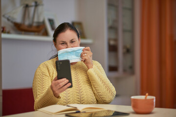 Senior woman in yellow sweater looking at smartphone with mask