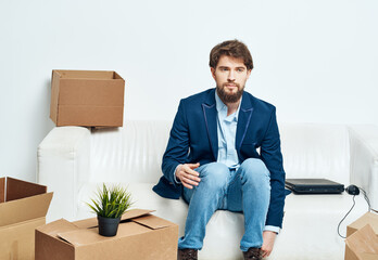 A man sits on the couch next to boxes unpacking a new moving location