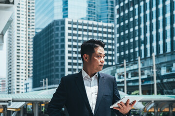 Fototapeta premium Handsome business man holding tablet in city outdoor with office building in the background