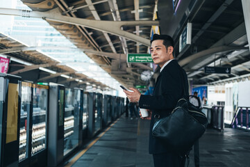 Business man holding a disposable coffee cup and mobile phone at train station