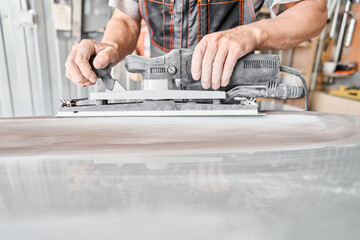 The mechanic works with a grinding tool. Sanding of car elements. Garage painting car service. Repairing car section after the accident.