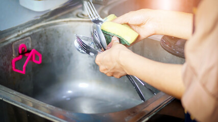 Woman washing spoons and forks in the kitchen close-up