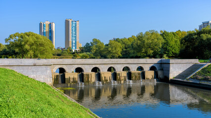 Stone dam-bridge over Dudergofsky canal with high-rise residential buildings on background at sunny autumn day