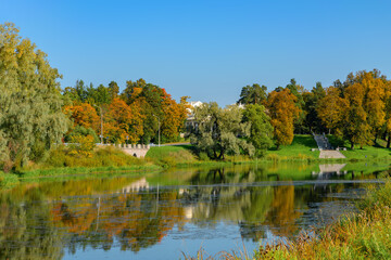 Fototapeta na wymiar Bright colorful autumn landscape, trees near river and blue sky, Bolshoy Kamenny bridge-dam and Mariental Staircase, which connects the pond to the site opposite the Imperial Palace in Pavlovsk