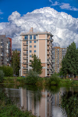 Public city park with pond and reeds and multi-storey dwelling buildings behind under blue sky with amazing clouds at sunny autumn day
