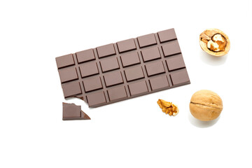 A bar of natural dark chocolate on a white background with a broken piece near nuts