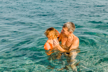 Fototapeta na wymiar Grandfather playing with toddler girl in sea