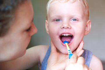 Mom teaches and helps her three-year-old son to brush his teeth.