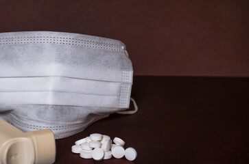 A white medical mask next to pills and an inhaler on a dark surface.