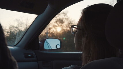 Fototapeta na wymiar A girl with glasses rides in the car in the front seat and looks into the distance. Back view.