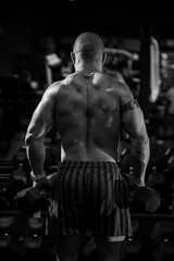 Fototapeta na wymiar Muscular shirtless man doing dumbbell exercises as part of his bodybuilding workout. Fitness motivation, sports lifestyle, health, athletic body, body positive