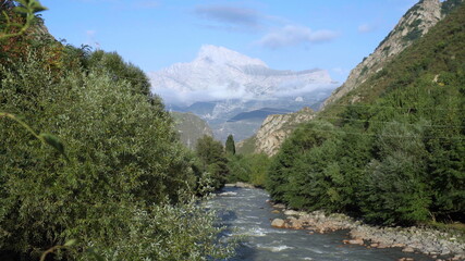 Fototapeta na wymiar The blue mountain river flows against the background of a snowy mountain. Travel to the mountains.