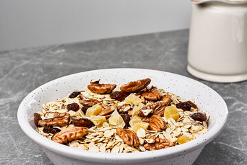 Muesli or granola with dried fruits and pecans nuts in white bowl on gray stone table. Healthy breakfast. Kinfolk style.