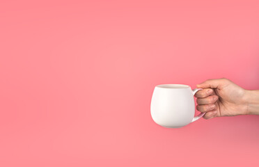 A woman's hand holds a white mug on a pink background. Background with space to copy, side view.