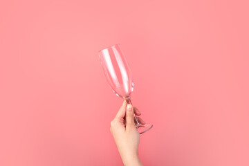 Hand holding a champagne glass on a pink background. Holiday background with space to copy.