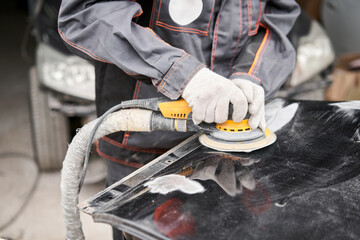The mechanic works with a grinding tool. Sanding of car elements. Garage painting car service....