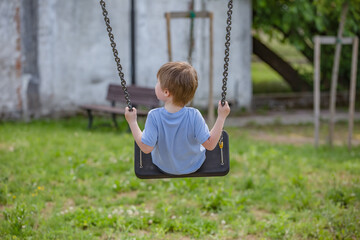 Little boy ride on a swing in the child playground. Little baby boy hand holding tightly on a metallic chain while going on a swing at a playground. Rear view