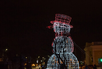 Snowman made of glowing garlands at night. Christmas and New Year street decoration