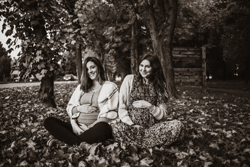 Sepia photo of two beautiful pregnant ladies relaxing in the park