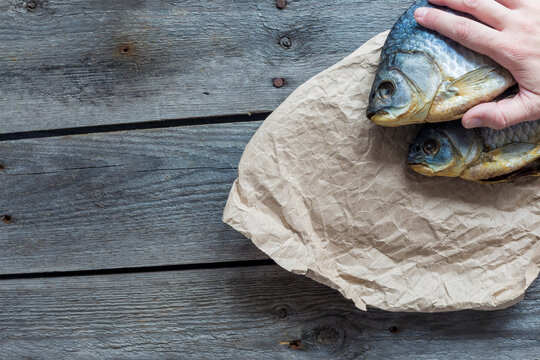 Hand holds Dried Volga bream vobla in a crumpled kraft paper roll