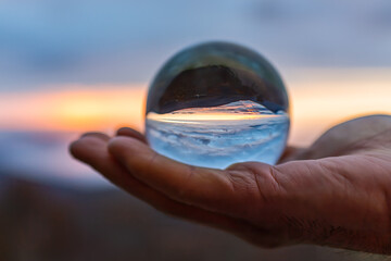 Person hand holding crystal glass ball view of round globe with reflection of fog mist clouds over...