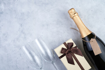 Christmas background with a bottle of champagne, wine glasses and a gift box on a gray background....