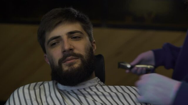 A bearded man trims his beard in a barber shop. Man hairdresser combing hair and cutting with a trimer