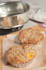 from view, medium distance of freshly baked peach streusel coffee cake in metal forms, cooling on parchment paper on a wood cutting board
