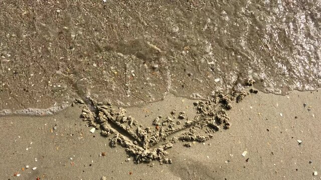 Sea waves gradually wash away the painted heart on the sandy beach