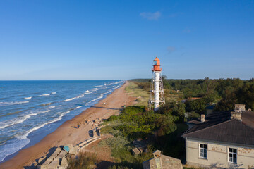 Aerial view of lighthouse with red top and white base. Blue sky and sea. Pape lighthouse