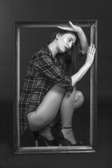 Studio black-and-white photo of a young woman with long brown hair in a plaid shirt and bare legs