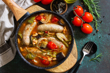 Stew smoked sausages with of beans, vegetables and tomato sauce in the pan on a stone countertop. Top view flat lay background.