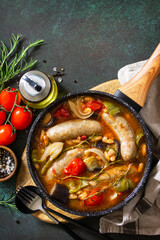 Stew smoked sausages with of beans, vegetables and tomato sauce in the pan on a stone countertop. Top view flat lay background. Copy space.